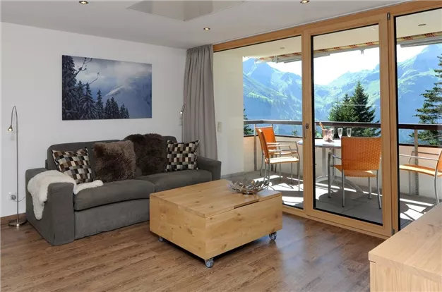 A modern living and dining room with large windows and a view of the mountains. Cozy furniture and a wooden coffee table create an inviting atmosphere.