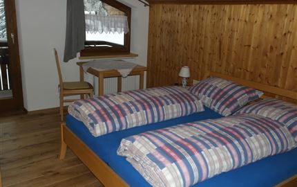 Ein gemütliches Schlafzimmer mit einem Doppelbett und Holzverkleidung. Ein kleiner Tisch und ein Stuhl ergänzen die Ausstattung.