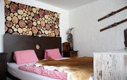 Ein gemütliches Schlafzimmer mit einem Holzstamm-Muster an der Wand. Es gibt ein Bett mit karierten Bettwäsche und rustikalen Dekorationen.
