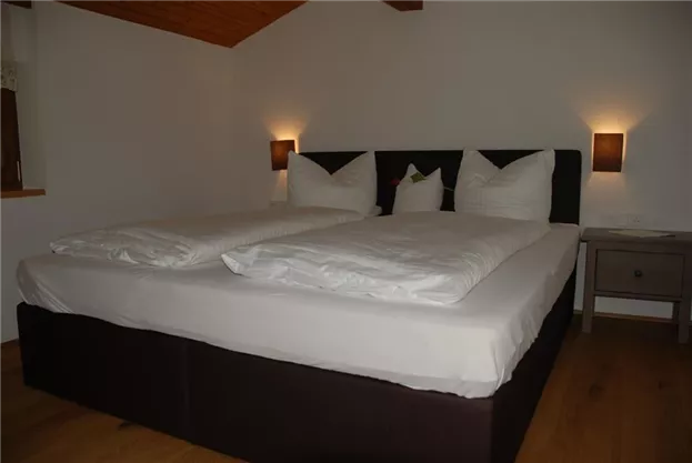 A cozy bedroom with a large double bed and two pillows. Soft bedding and gentle light create a relaxed atmosphere.