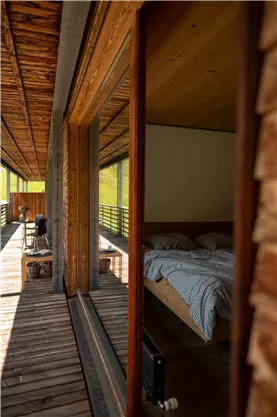 A modern room with a bed and wooden paneling. The view leads to a terrace surrounded by nature.