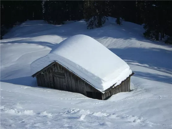 Eine kleine Holzhütte ist unter einer dicken Schneeschicht verborgen. Die Umgebung ist winterlich und friedlich.
