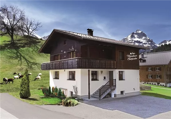 A cozy chalet in the Alps, surrounded by green meadows and mountains. Cows graze peacefully near the house.