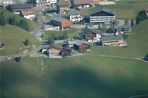 Eine malerische alpine Landschaft mit mehreren Häusern und sanften Hügeln. Die Umgebung ist grün und zeigt eine ruhige, ländliche Atmosphäre.