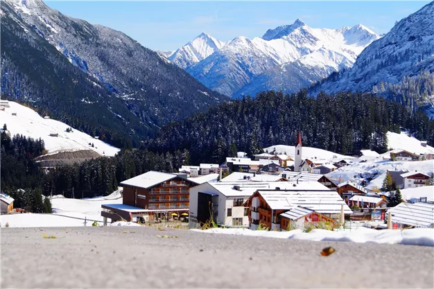 A snowy mountain landscape with a small village in the valley. The majestic mountains surround the idyll and the sky is clear and blue.