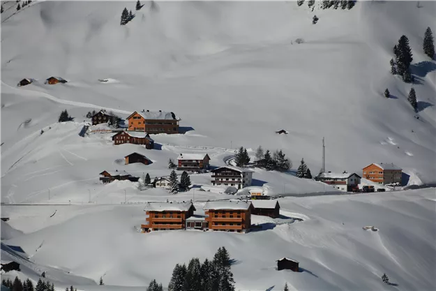 Eine verschneite Landschaft mit mehreren Chalets und Bäumen. Die Hütten sind umgeben von weißem Schnee und einem blauen Himmel.