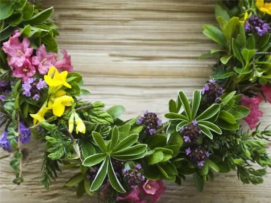 Ein schöner Blumenkranz mit bunten Blumen und grünem Laub. Die natürliche Deko liegt auf einer Holzoberfläche.