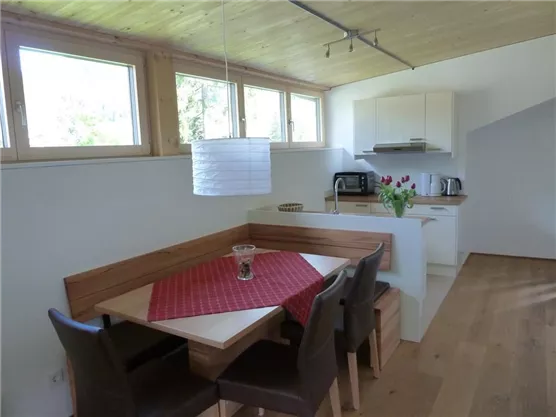 A modern kitchen with a cozy dining area. The table is decorated with a red cloth and fresh flowers.