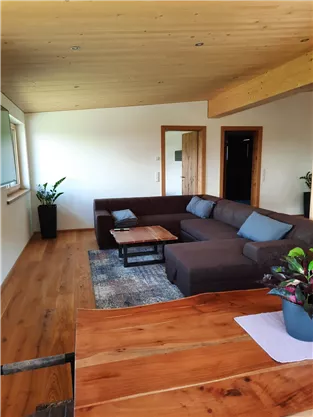 A cozy living room with a large sofa and a wooden table. Plants give the room a pleasant atmosphere.