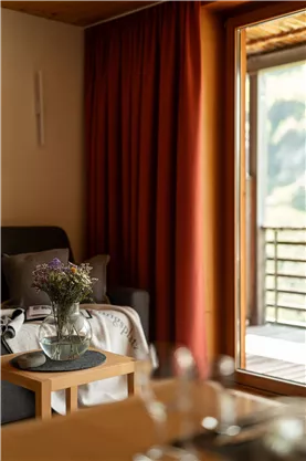 A cozy living room with a sofa and a table. In front of a window, you can see a bright view and fresh flowers in a vase.